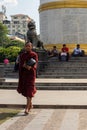 Young male monk asking for alms, food or money. Dressed in traditional red clothes, shaved head. Carrying alm bowl. Walking