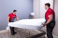 Young Male Movers Placing The Mattress Over The Bed