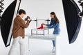 Young male photographer taking photo of stylish red shoes on white platform in photostudio with modern equipment