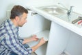 Young male plumber lying on floor fixing sink in bathroom Royalty Free Stock Photo