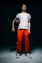 Young male prisoner wearing orange pants and cuffs holding basketball ball Royalty Free Stock Photo