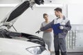 Young male repairman explaining car engine to female customer in automobile repair shop