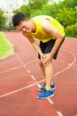 Young male runner suffering from knee injury on the track