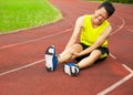 Young male runner suffering from leg cramp on the track