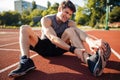 Young male runner suffering from leg cramp on the track