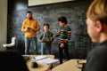 A Quality School. Young male science teacher standing near the blackboard, holding tablet pc and looking at his students