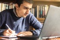 Young Caucasian male sitting at a desk working with a laptop taking notes on a webinar or concept training course the computer and Royalty Free Stock Photo