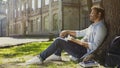 Young male sitting under tree with book looking around, having pleasant thoughts Royalty Free Stock Photo