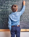 A young male student in a denim shirt and slacks writes complex math and physics equations on a classroom blackboard. Generative Royalty Free Stock Photo