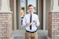 Young male student holding a diploma in front of a house while wearing a dress shirt and a tie.