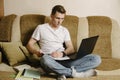 A young male student sits at home on the couch and does homework on a laptop and writes in a notebook.Distance learning Royalty Free Stock Photo