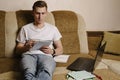 A young male student sits at home on the couch and does homework on a laptop and writes in a notebook.Distance learning Royalty Free Stock Photo