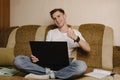 A young male student sits at home on the couch and does homework on a laptop and writes in a notebook.Distance learning Royalty Free Stock Photo