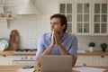 Young male studying at kitchen pondering distracted from laptop screen