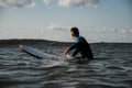 Young male surfer in wetsuit sitting on surfboard and waiting for wave to stand up Royalty Free Stock Photo