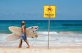 Young male is about to surf with a big sign forbidding to swim in that area