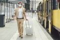 Male tourist in mask carrying luggage at tramway stop Royalty Free Stock Photo