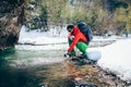 Young male tourist fillings water into the bottle from a river in the mountains.