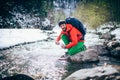 Young male tourist fillings water into the bottle from a river in the mountains.