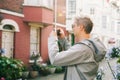 Young male tourist filming video or taking photo pictures on mobile phone during walking in the cottagecore residential