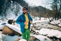 Young male tourist straightens his jacket near a river in the mountains.