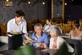 Young male waiter serving dish to elderly couple in restaurant Royalty Free Stock Photo