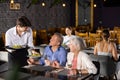 Young male waiter serving dish to elderly couple in restaurant Royalty Free Stock Photo