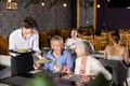 Young male waiter serving dish to elderly couple in restaurant Royalty Free Stock Photo