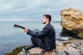 Young man with acoustic guitar playing on beach surrounded with rocks on rainy day Royalty Free Stock Photo