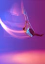 Young man, acrobat training with aerial ribbons against gradient blue purple studio background in neon with mixed lights Royalty Free Stock Photo