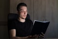 Young man or an adult guy in the dark reads a glowing book. The concept of teaching is light, not teaching is darkness Royalty Free Stock Photo