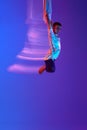 Young man, aerial gymnast, acrobat training with aerial tissue against gradient blue purple background in neon with