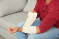 Young man applying bandage on injured arm at home, closeup.