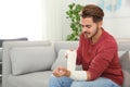 Young man applying bandage on injured arm at home, space for text Royalty Free Stock Photo