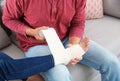 Young man applying bandage on woman`s injured leg at home, closeup.