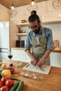 Young man in apron peeling, cutting garlic while preparing dinner, standing in the kitchen. Cooking at home concept Royalty Free Stock Photo