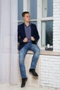 Young man with an arrogant expression. Sits by the window on the windowsill Royalty Free Stock Photo