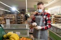 Young man as a market leader with tablet PC in the fruit section in the supermarket, employee in protective mask using