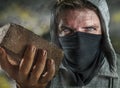 Young man as ultra and radical anarchist rioter . furious antifa protester in face mask throwing brick hostile on street on