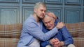 Young man asking for apologizes to offended stressed elderly senior father sitting together on couch