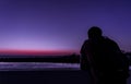 Young man from the back with a backpack looks at the purple sunset over the sea Royalty Free Stock Photo