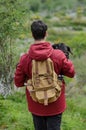 Young man with backpack carries his dog in his arms
