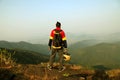 Young man with backpack and helmet standing with raised hands on top of a mountain and enjoying valley view Royalty Free Stock Photo