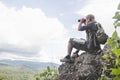 Young man with backpack and holding a binoculars sitting on top of mountain, Hiking and tourism concepts Royalty Free Stock Photo