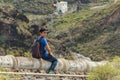A young man with a backpack seats on the concrete aqueduct in the west side of Tenerife near the Adeje village. Hiking by the