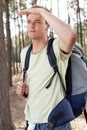 Young man with backpack shielding eyes in forest