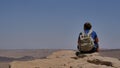 Young man with backpack sitting on cliff`s edge and enjoying the desert view Royalty Free Stock Photo