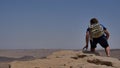 Young man with backpack sitting on cliff`s edge and looking at the desert Royalty Free Stock Photo