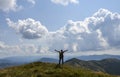 Young man with backpack standing with raised hands on peak of mountain and enjoying view Royalty Free Stock Photo