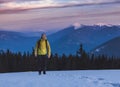 Young man with backpack standing on the snow and looking aside with beautiful mountains on the background Royalty Free Stock Photo